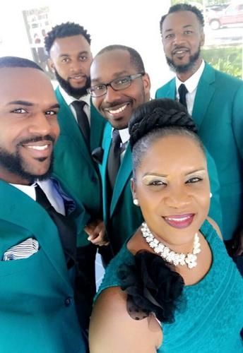 Five people in teal suits smiling for a selfie indoors