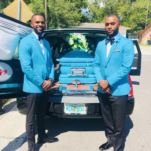 Two men in blue suits standing by an open hearse with a blue casket inside