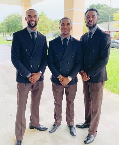 Three men in dark suits stand together outdoors under a covered walkway.