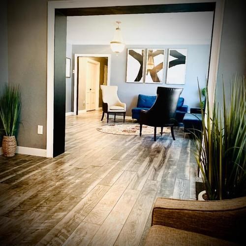 Modern living room with wood floors, blue chairs, abstract wall art, and large doorway view