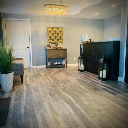 Spacious gray living room with wood floors, a small fireplace mantel, and a black TV cabinet with lanterns.