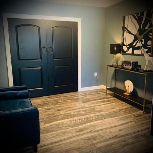 Modern living room with navy double doors, light wood floor, blue sofa, and black console table with abstract art