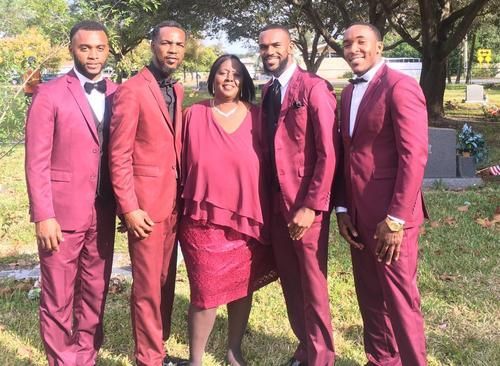 Five people in matching burgundy outfits posing outdoors on grass under trees