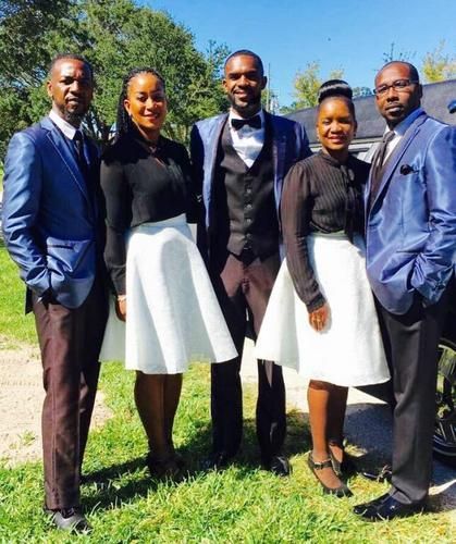 Five people standing together outdoors on grass, dressed in formal blue, black, and white attire.