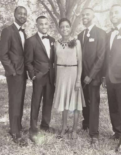 Five people posing outdoors, four in suits and one in a dress, standing in front of a tree.
