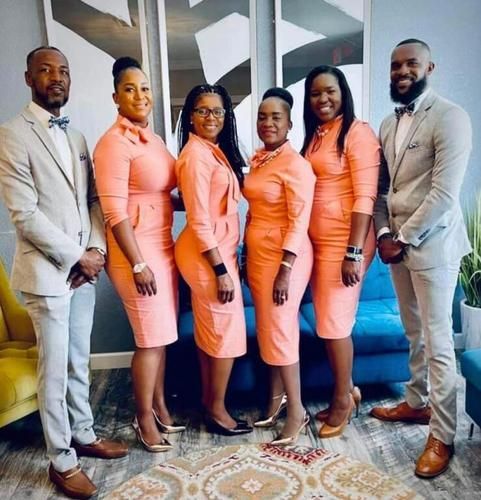 Five adults posing indoors in coordinated peach and beige outfits by a blue couch