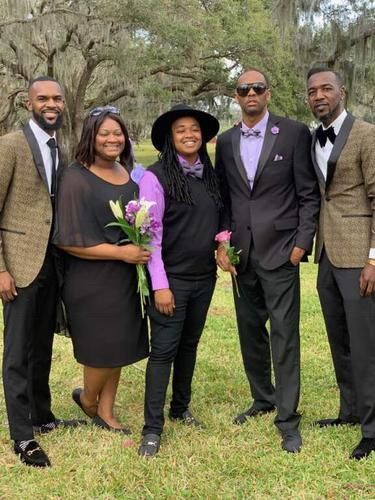 Five people posing outdoors on grass, dressed in formal black and purple attire.