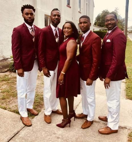 Five people in matching burgundy and white formalwear posing outdoors on a sidewalk.