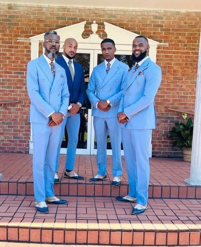 Four men in light blue suits posing on brick steps in front of a brick wall.