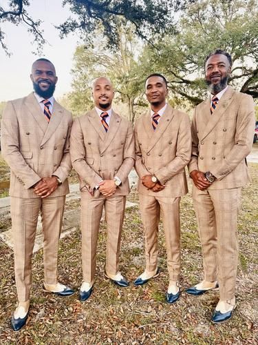Four men in tan suits standing outdoors under trees, posing together for a formal photo.