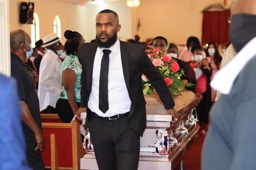 Man in black suit walking down church aisle past floral arrangements during a ceremony