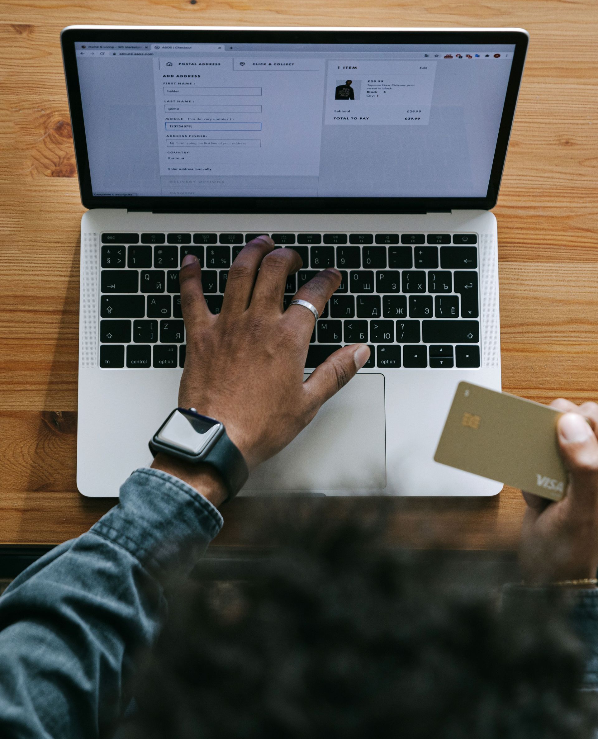 Person using a laptop while holding a credit card at a wooden desk.