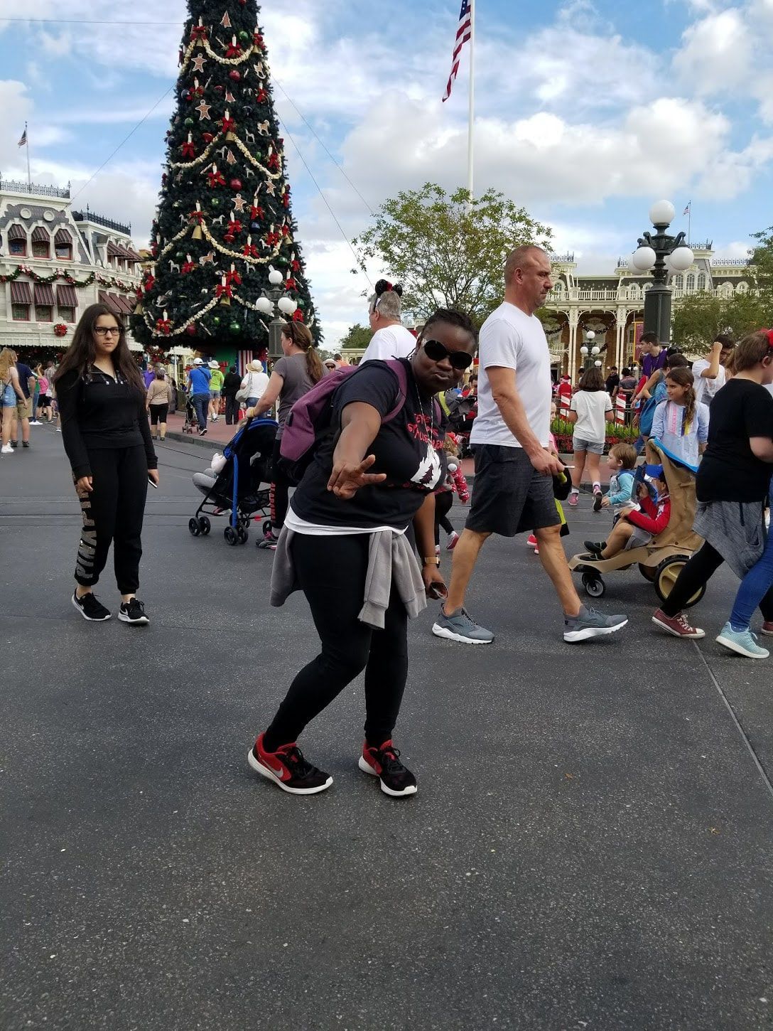 People walking in a theme park plaza beside a large decorated Christmas tree.