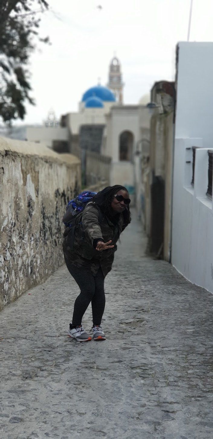 Person in dark clothing leaning forward on a narrow cobblestone street with buildings in the background.