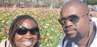 Two people smiling in sunglasses at a colorful flower garden.