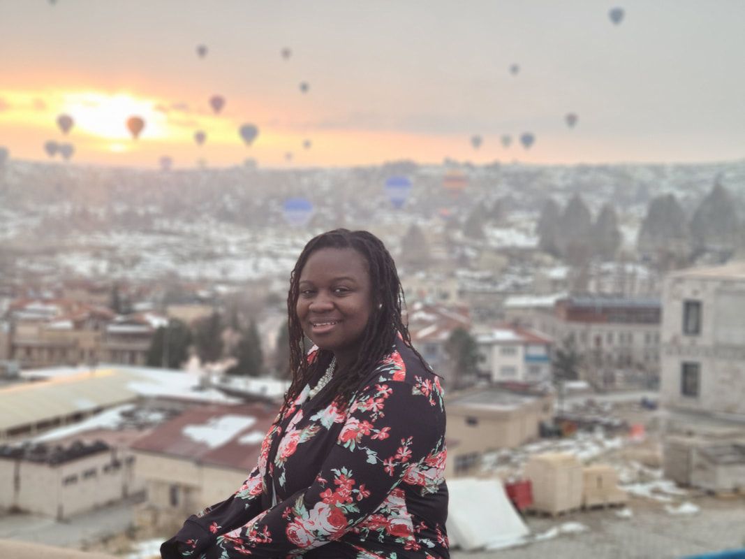 Smiling woman in floral jacket overlooking a snowy city at sunrise with hot air balloons in the sky