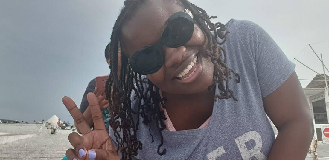 Smiling person in sunglasses flashing a peace sign on a beach with cloudy sky