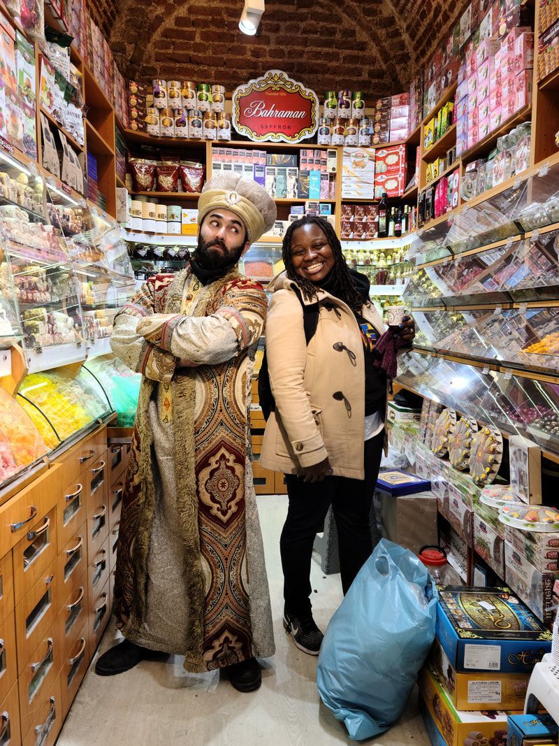 Two people stand in a crowded market aisle surrounded by colorful packaged goods.