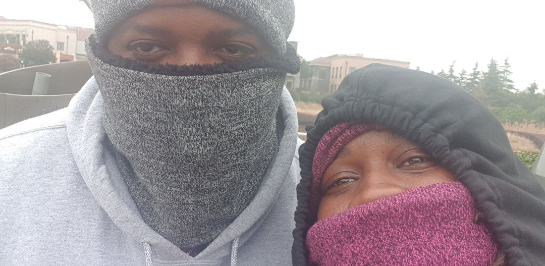Two people outdoors in winter, bundled in gray and pink face coverings with hoods up.