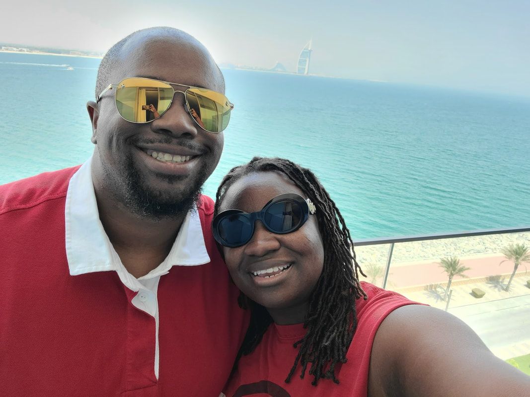 Two people smiling in red shirts and sunglasses by a turquoise ocean backdrop