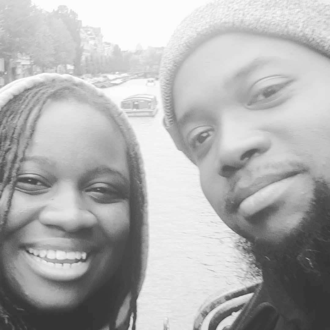 Two smiling people taking a selfie outdoors by a river on a cloudy day