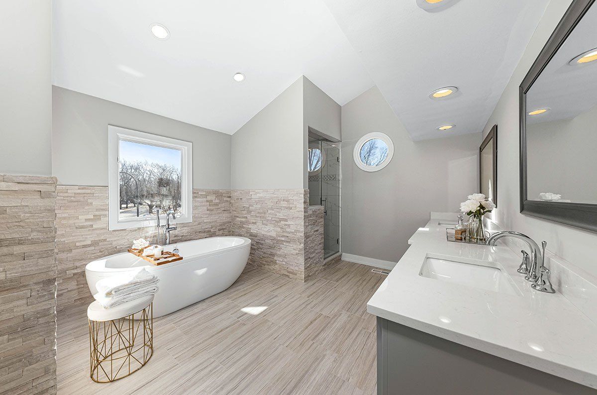 A bathroom with a tub , sink , mirror and window.
