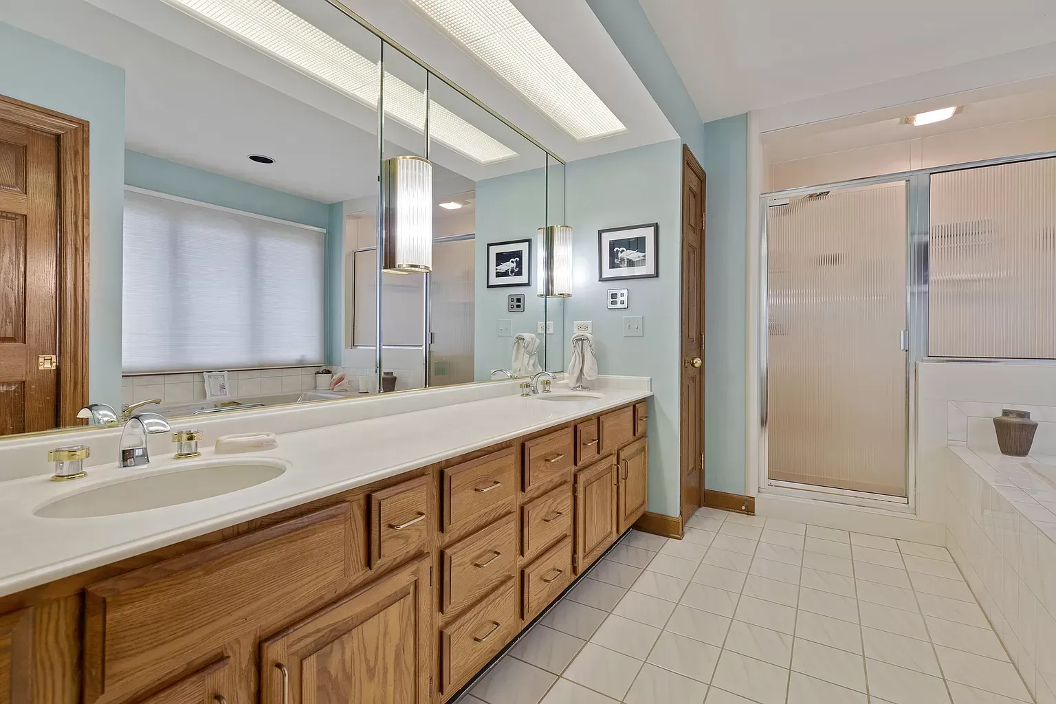 A bathroom with two sinks , a shower and a large mirror.