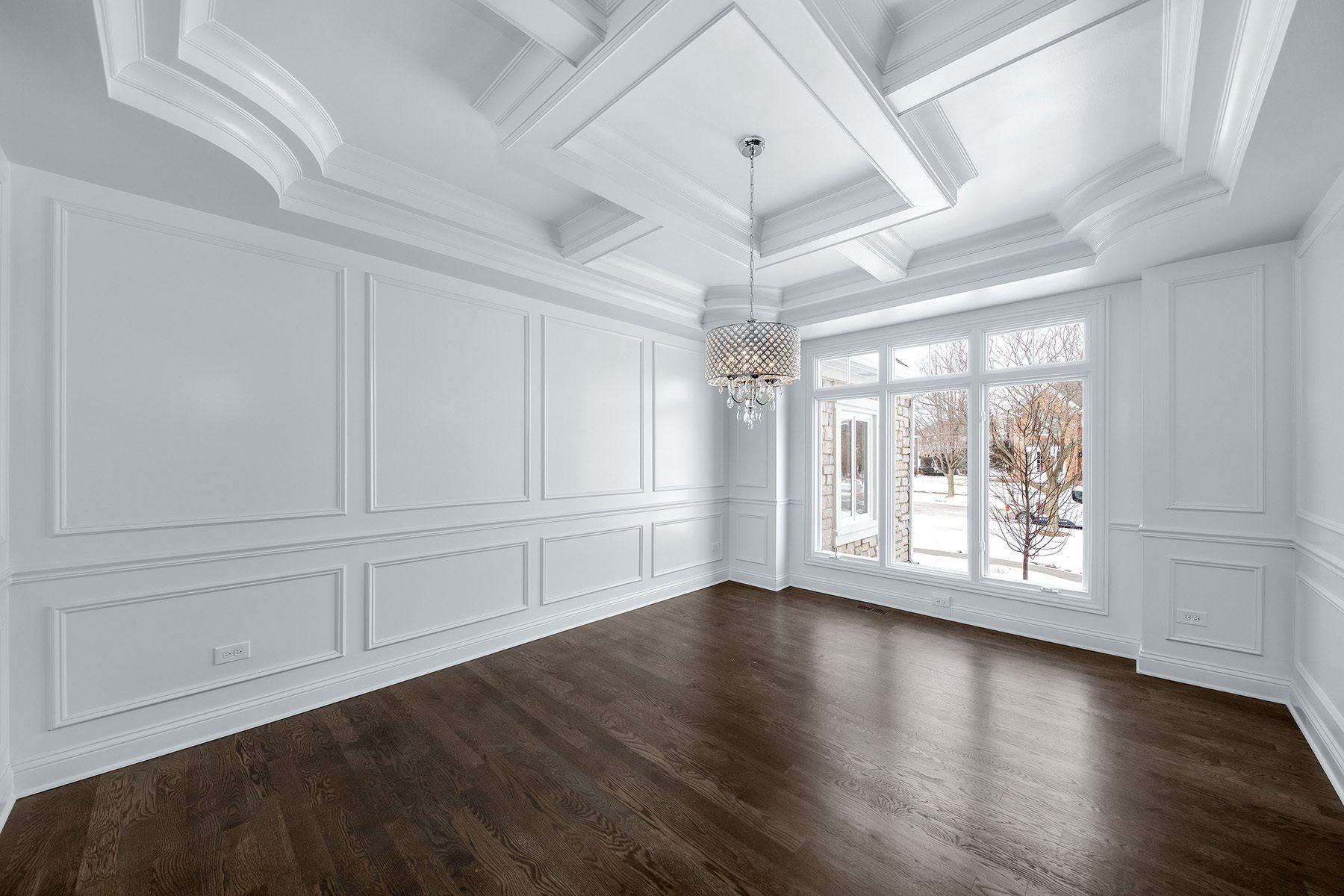 An empty room with hardwood floors , white walls , and a chandelier.