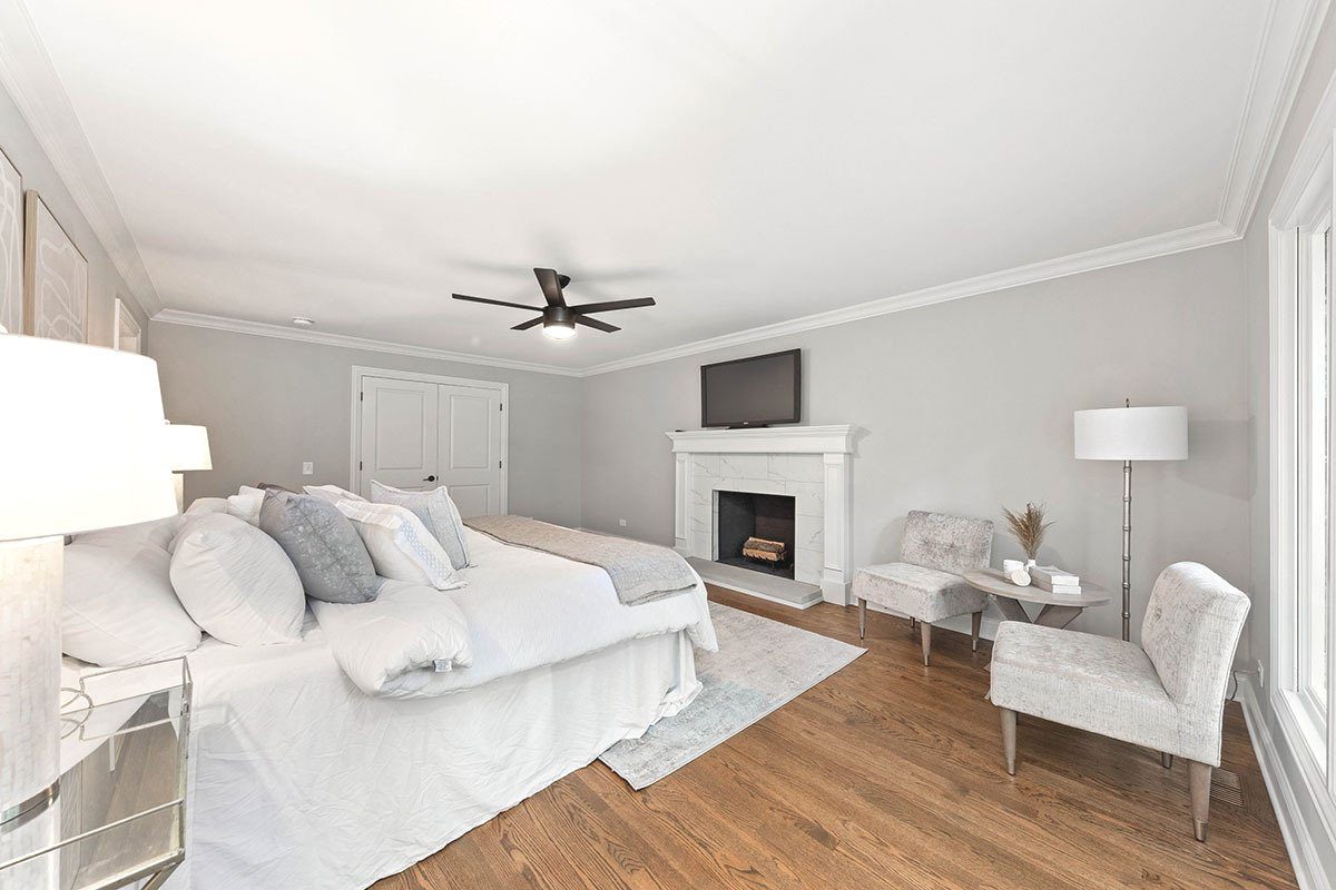 A bedroom with a bed , chairs , fireplace and television.