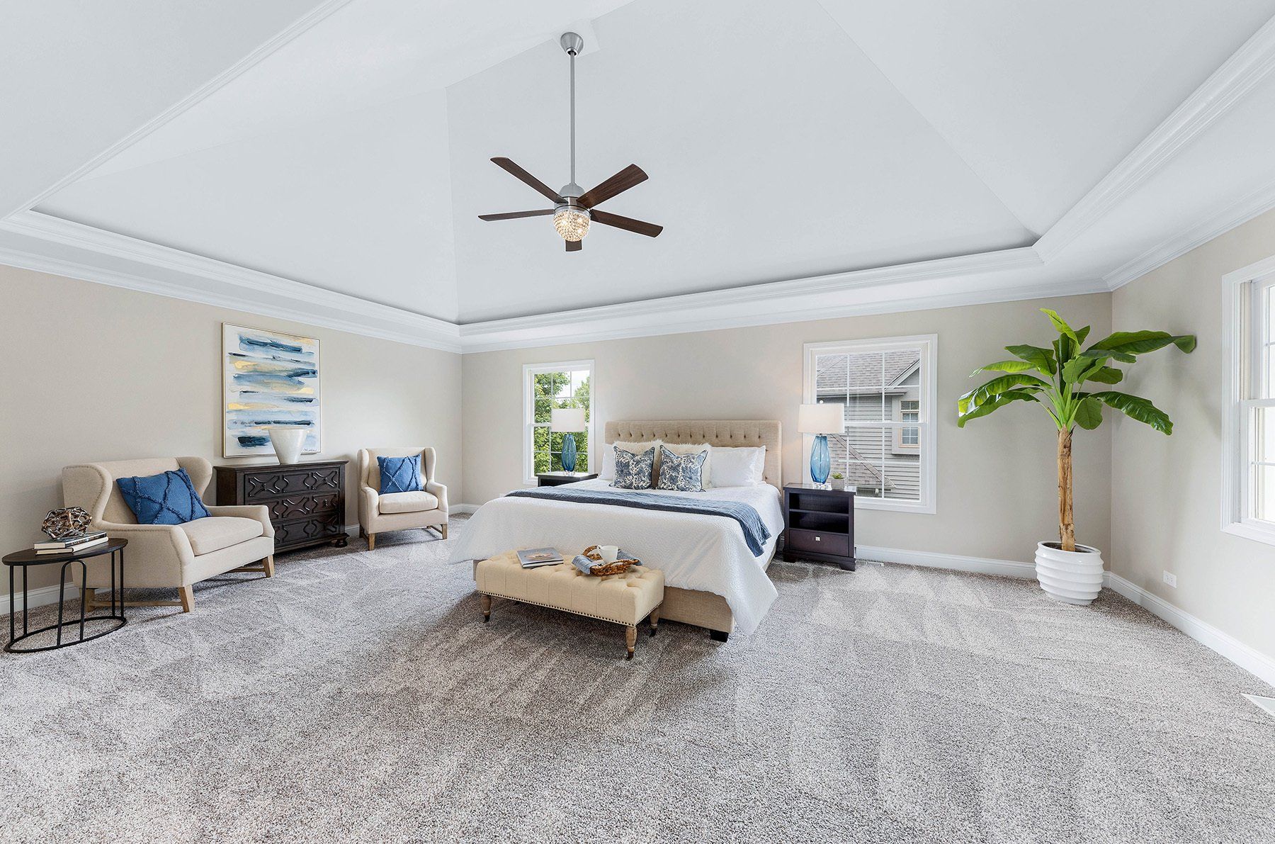 A bedroom with a bed , chairs , a ceiling fan and a palm tree.