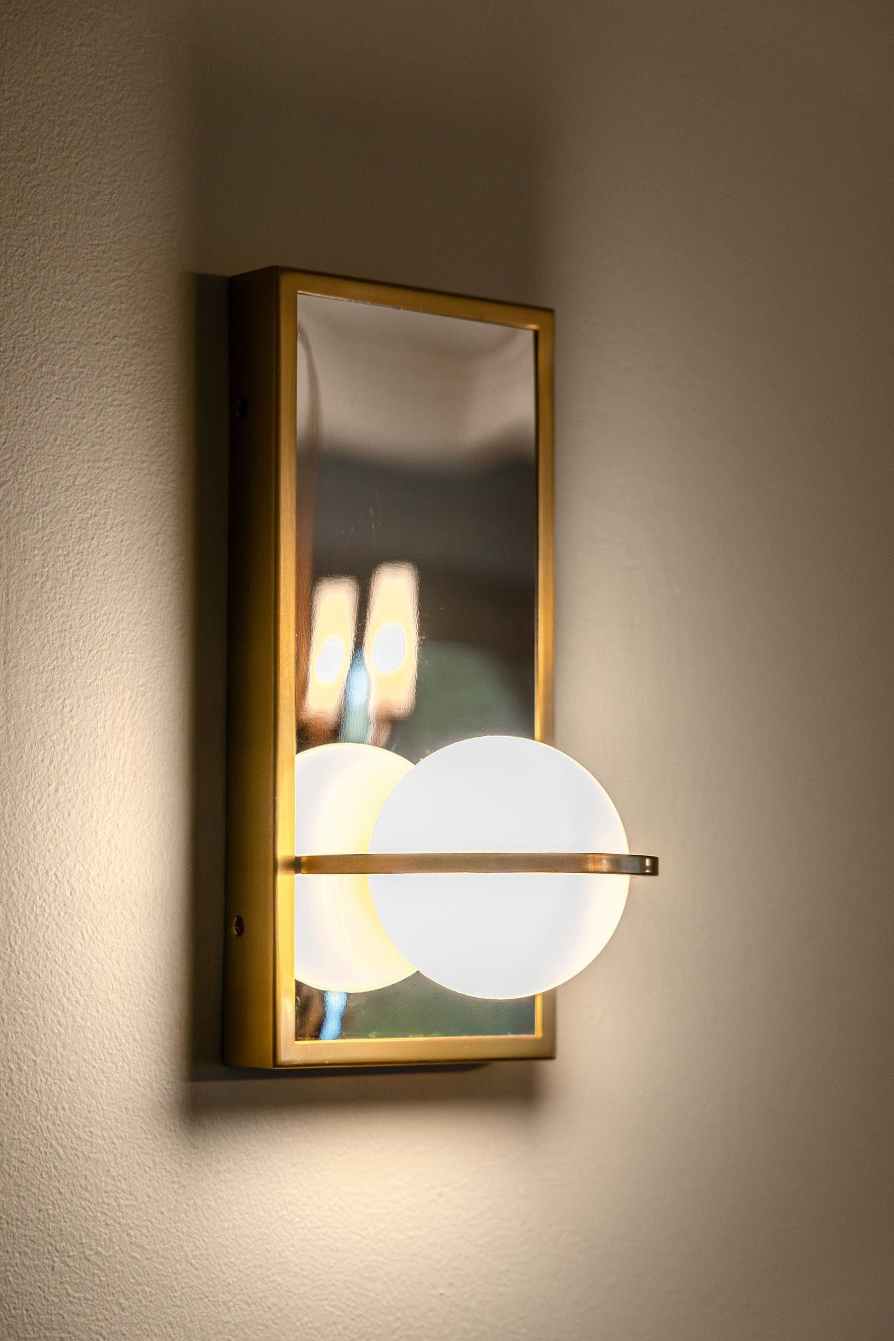 A wall light with a glass globe and a mirror on a wall.