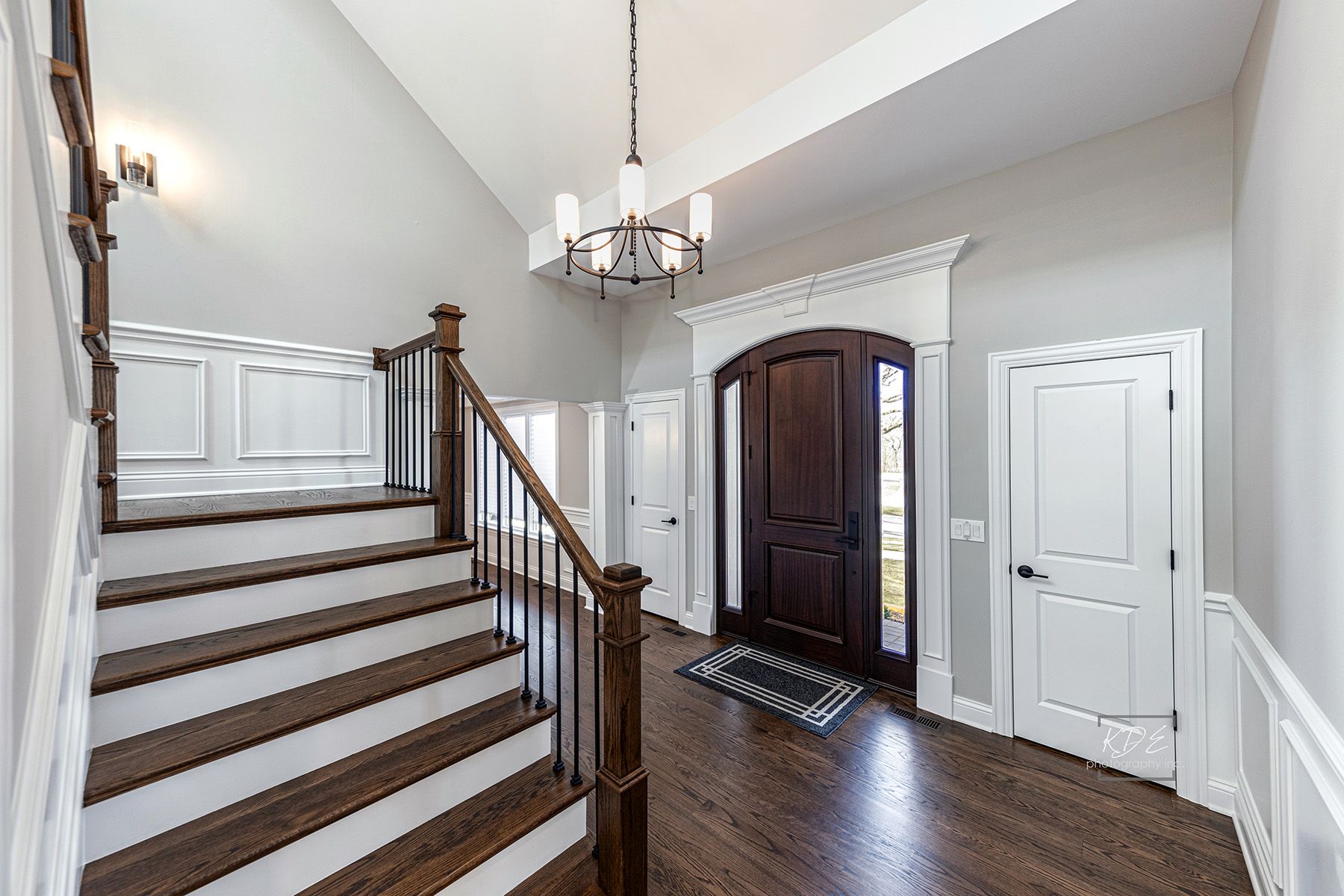 A hallway with stairs leading up to a door and a chandelier hanging from the ceiling.