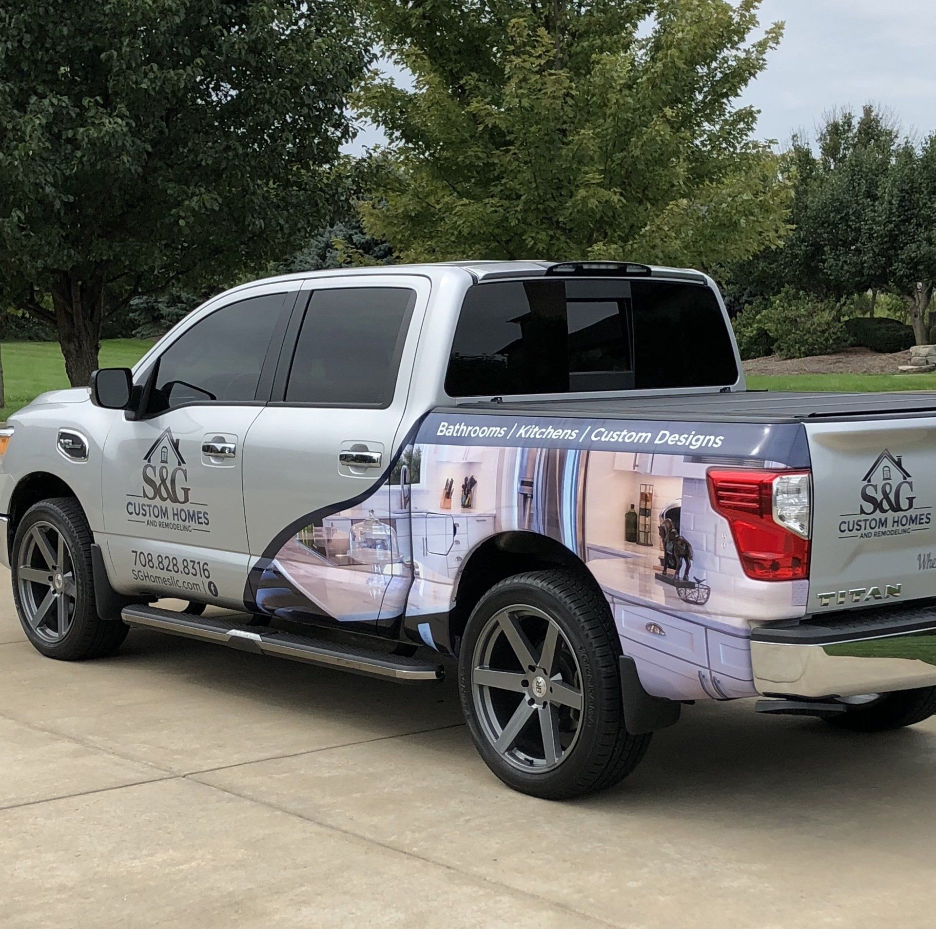 A truck with a kitchen wrap on the back is parked in a driveway.