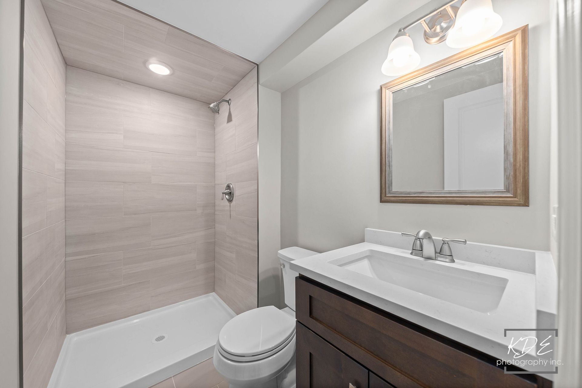 A bathroom with a toilet , sink , mirror and shower.