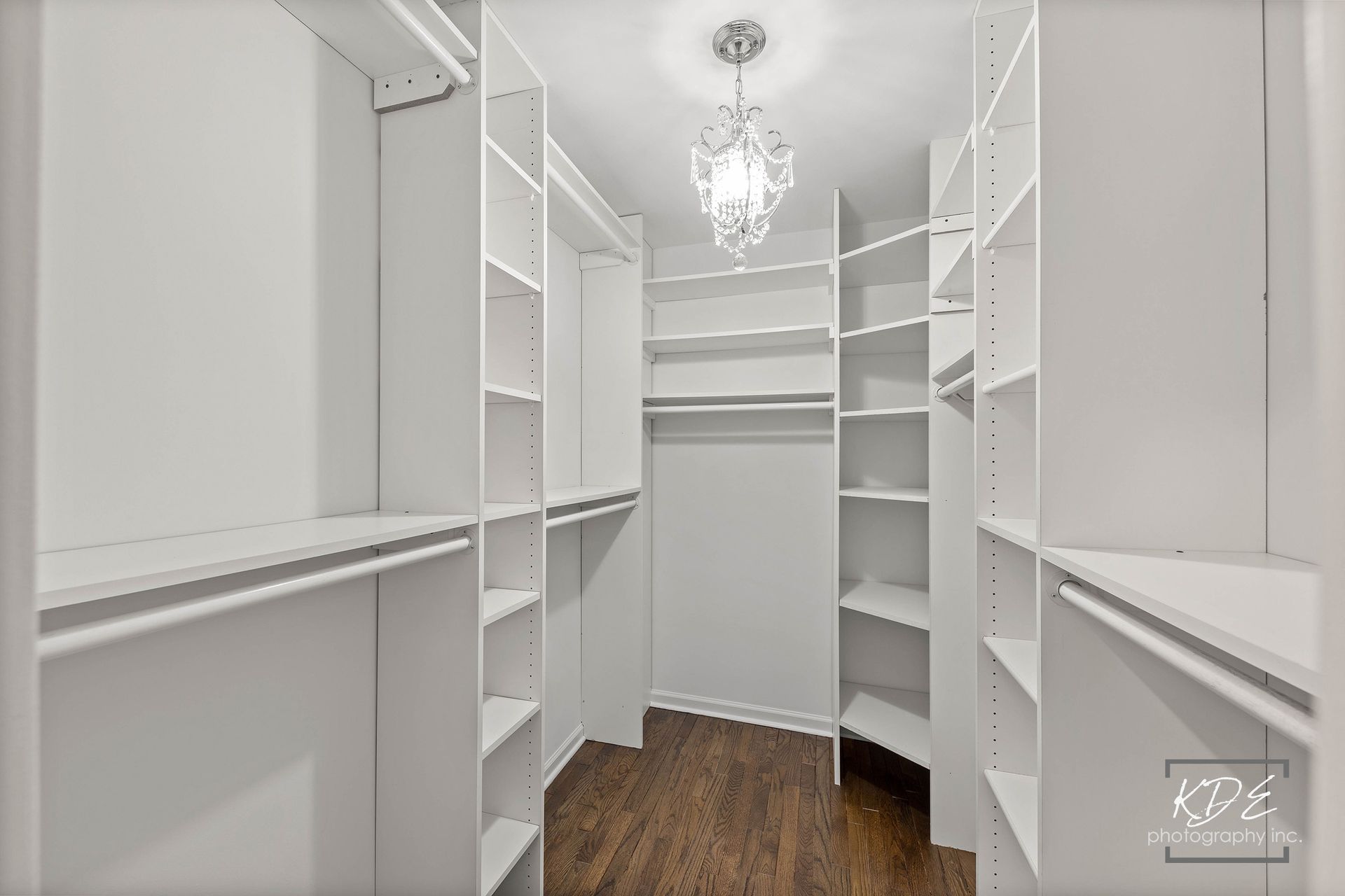 A walk in closet with white shelves and a chandelier.