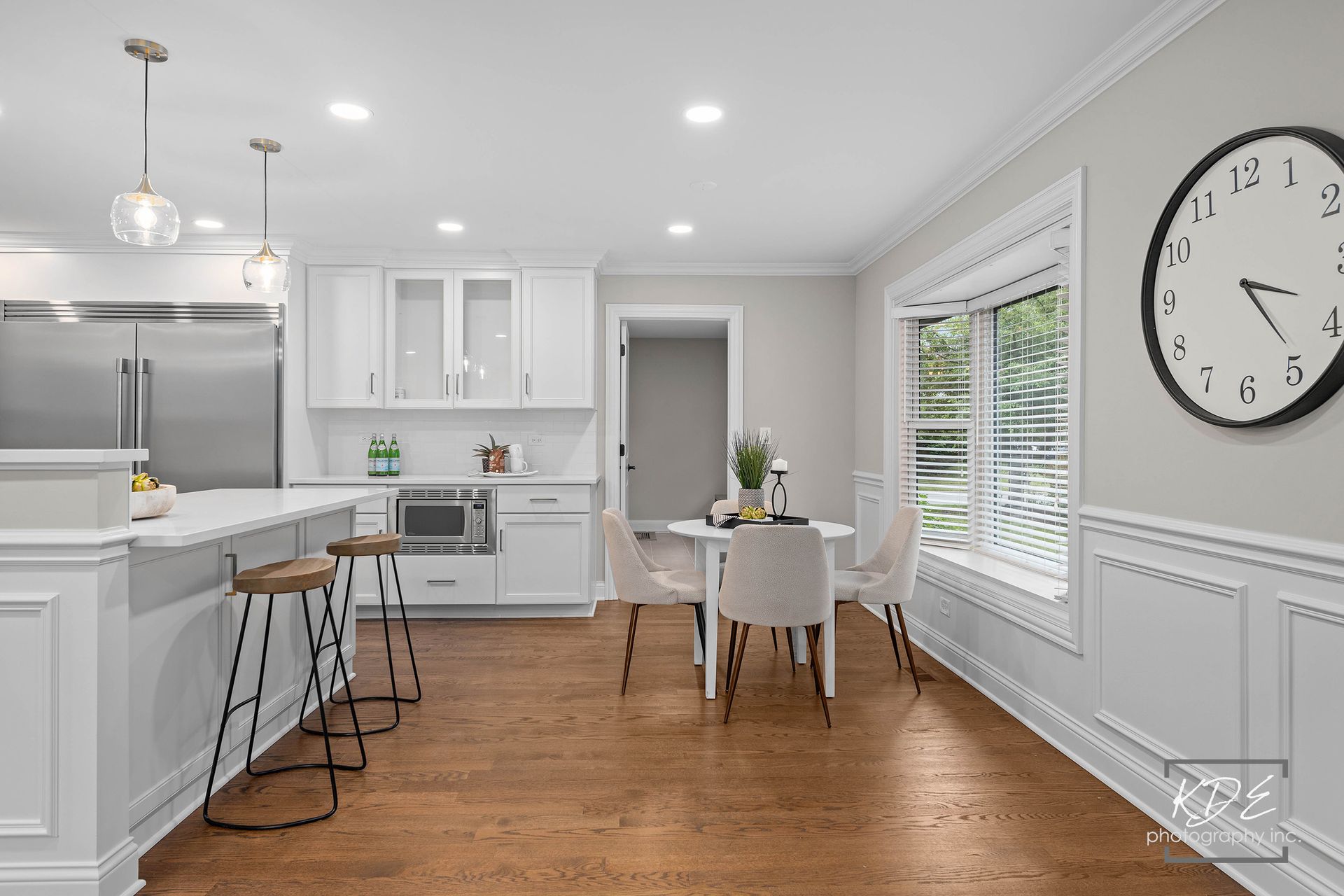 A kitchen with white cabinets and hardwood floors and a clock on the wall.