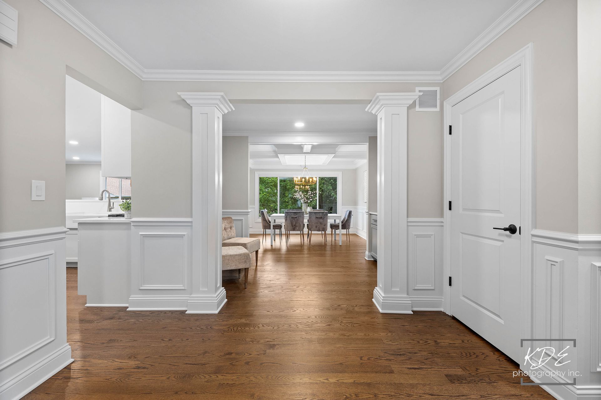 A hallway in a house with hardwood floors and white trim leading to a dining room.