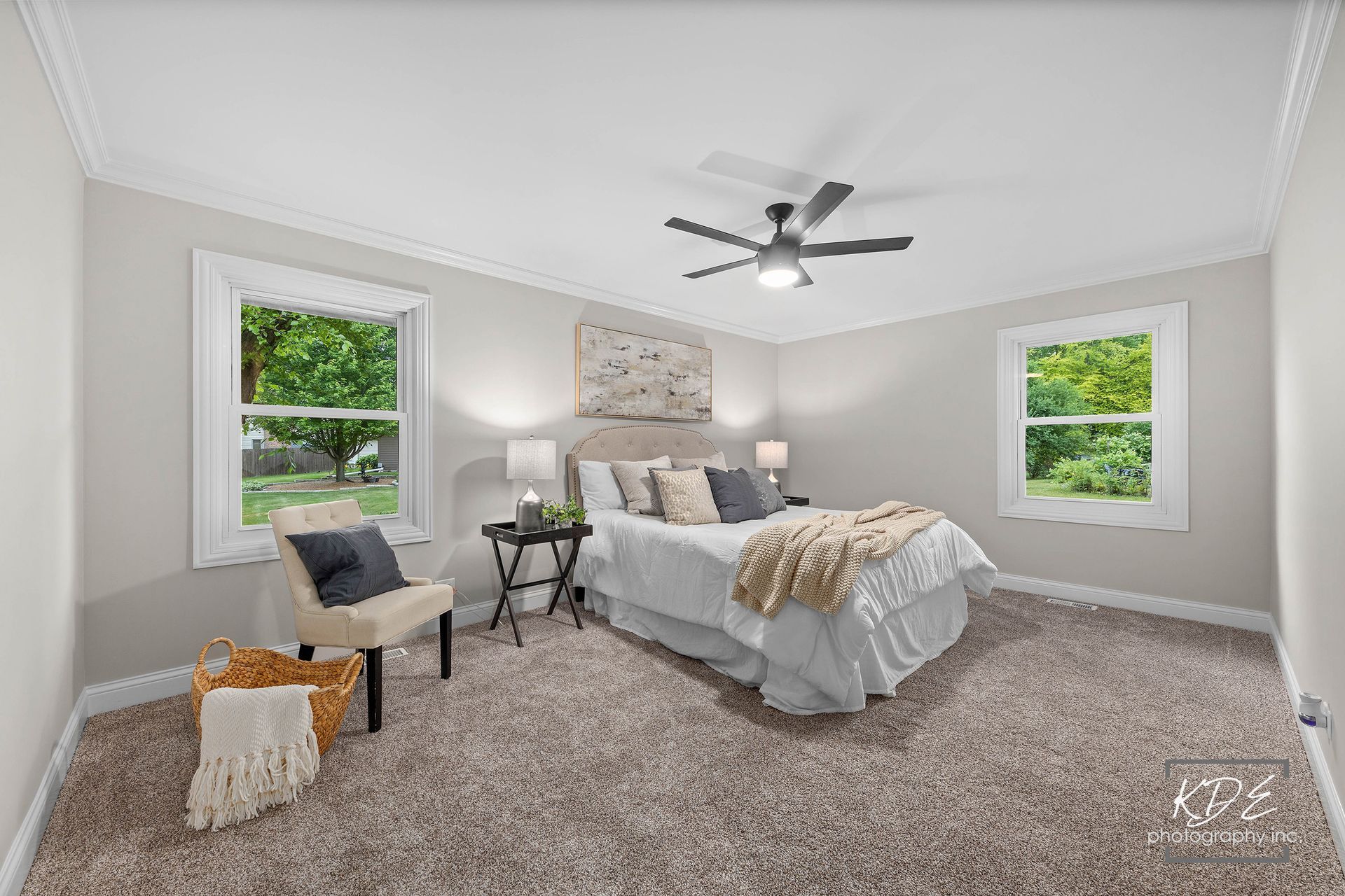 A bedroom with a bed , chair , table and ceiling fan.