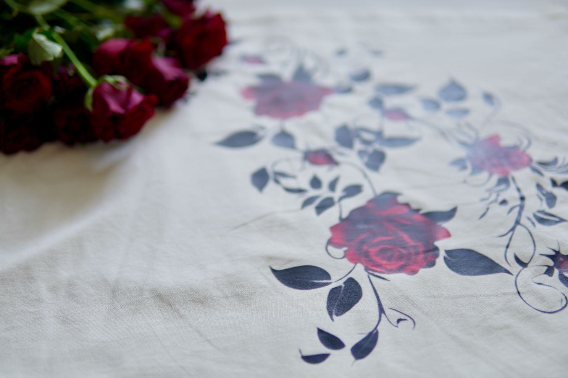 Red roses next to fabric with floral print of red roses and dark leaves.