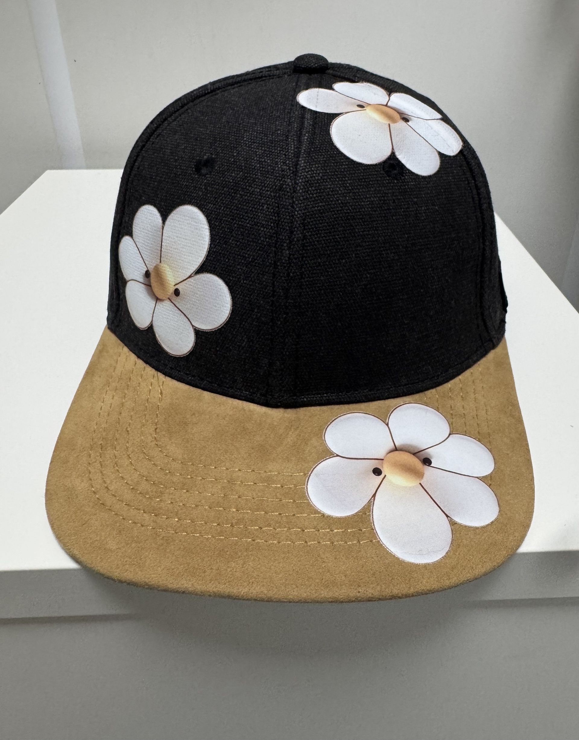 Black and tan baseball cap decorated with white daisies.