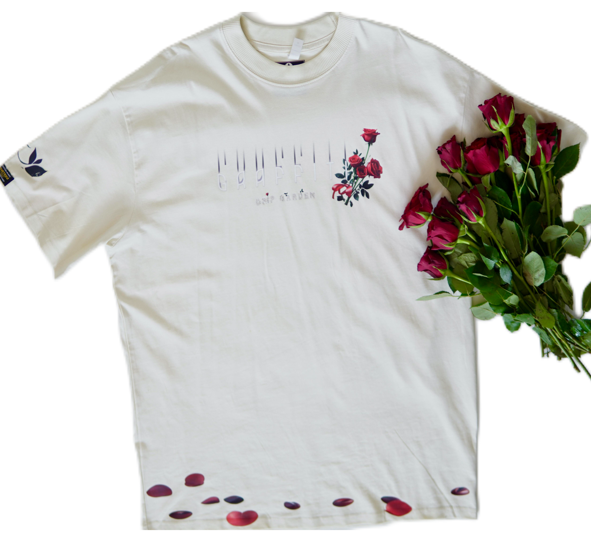 Off-white t-shirt with floral design, red roses to the side and petals scattered below.