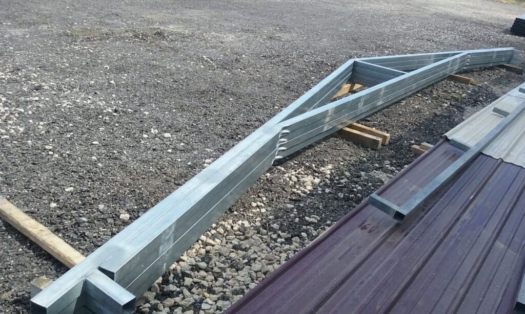 Damaged metal roof truss lying on gravel beside a corrugated roof edge