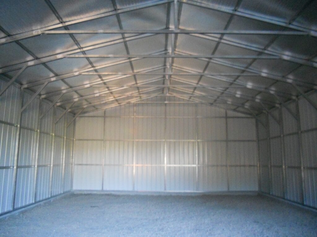 Empty metal warehouse interior with corrugated walls, arched roof, and gravel floor