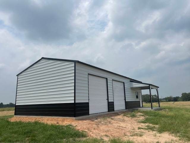 Metal storage building with gray siding and black trim on a dirt lot under cloudy skies