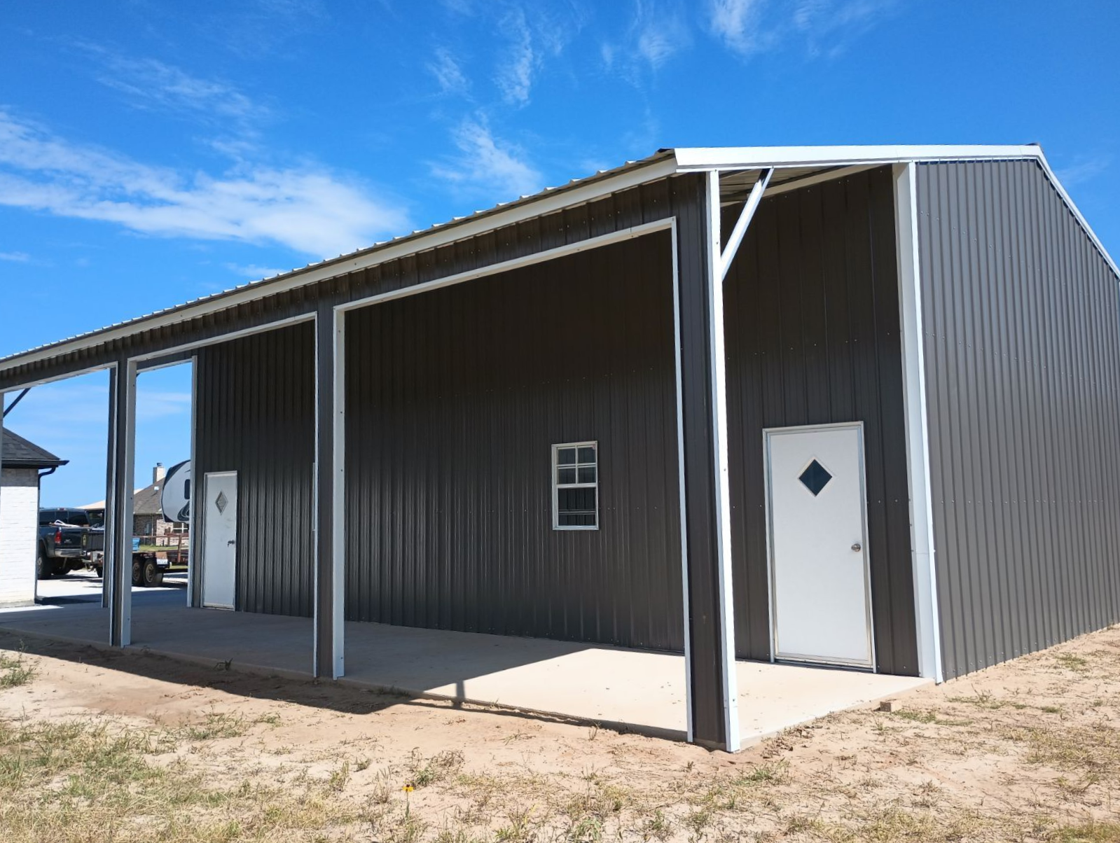 Metal-sided building with a covered porch, white doors, and blue sky overhead