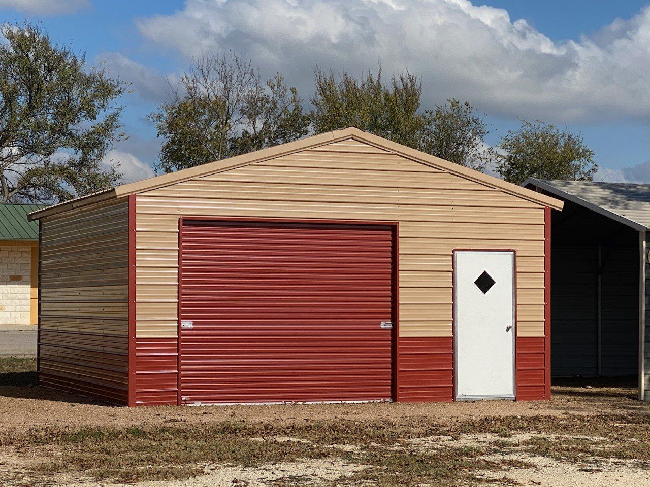 Small beige garage with red roll-up door and white side door on a grassy lot under a cloudy sky
