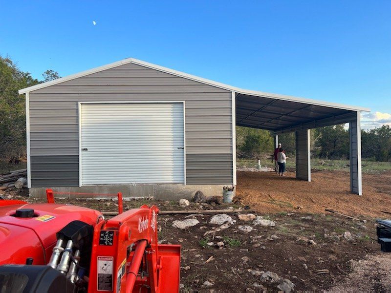 Gray metal garage with white roll-up door, red tractor in foreground, and a covered side bay on a dirt lot.