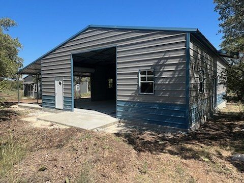 Blue-gray metal barn with open bay doors on a dirt lot under a clear sky