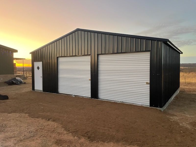 Black metal garage building with two white roll-up doors at sunset