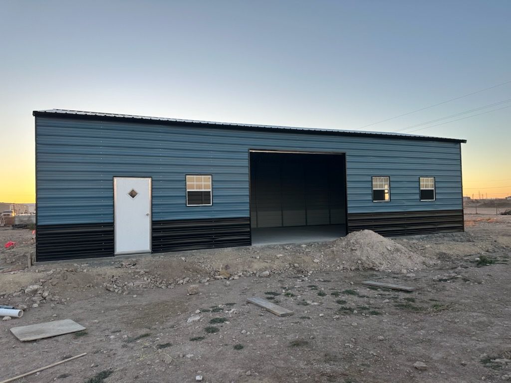 Blue metal building with white door and garage opening on a gravel lot at dusk